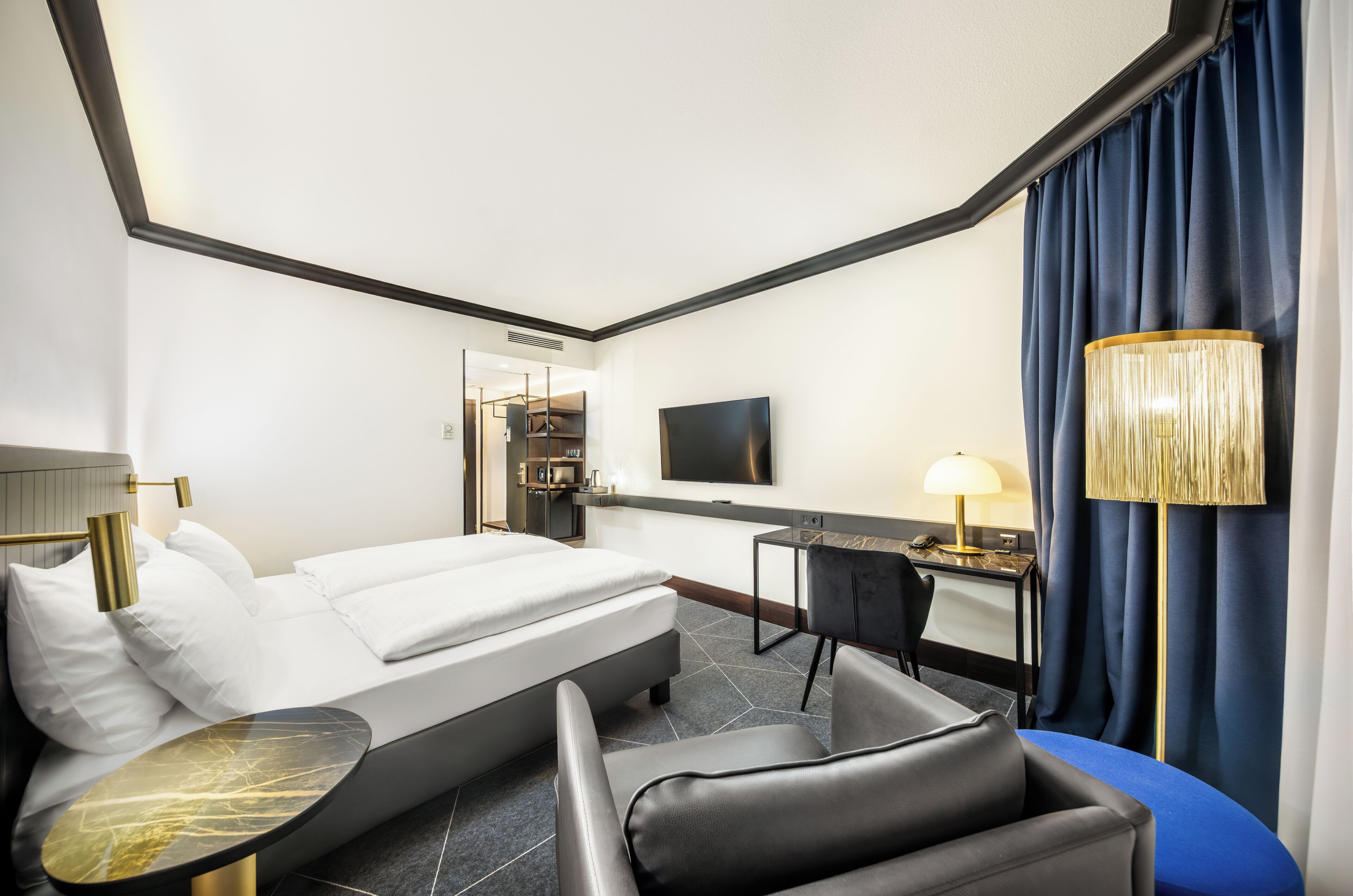 Una habitación de hotel con una cama, un escritorio, una silla, un televisor y una lámpara.