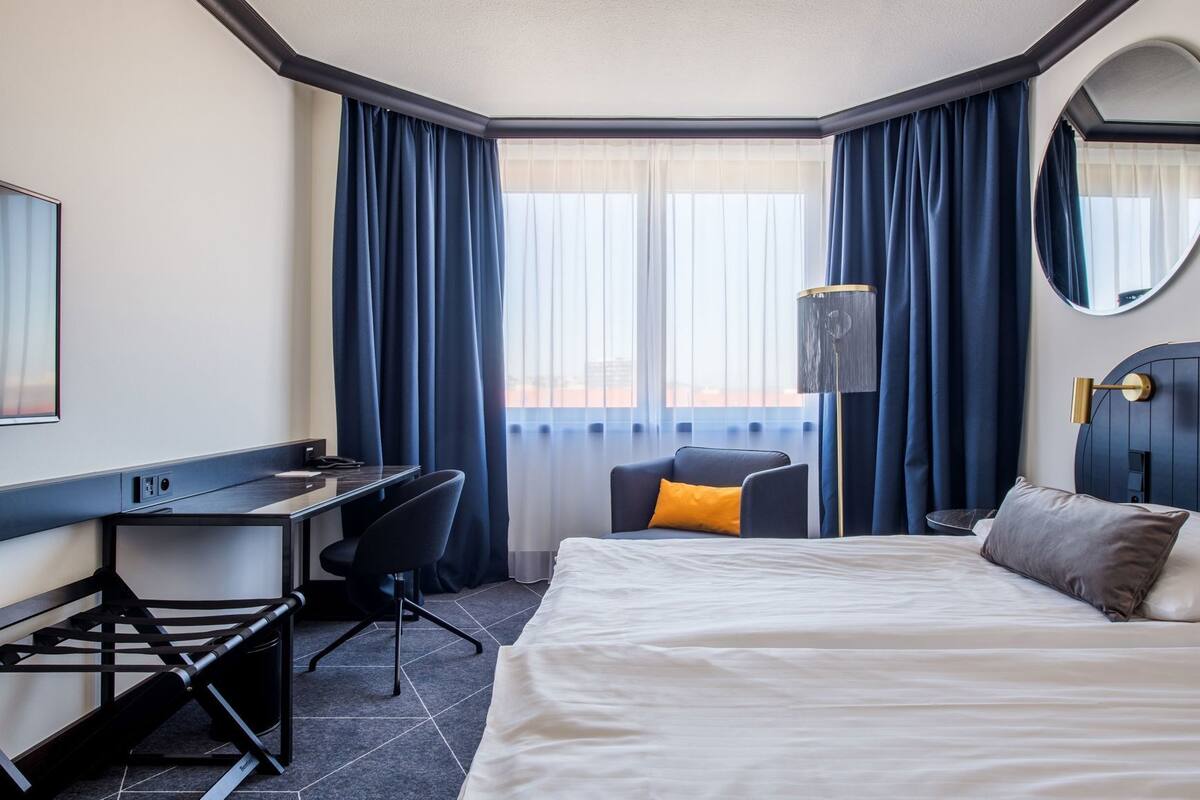 A hotel room with a bed, desk, chair, and a large mirror.