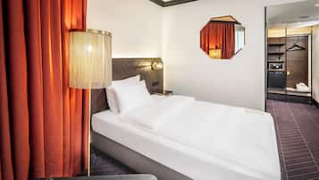 Habitación de hotel con cama, mesita de noche, lámpara, espejo y armario.