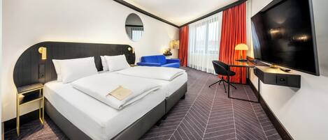 A hotel room with a large bed, a desk with a TV, a chair, and a desk lamp.