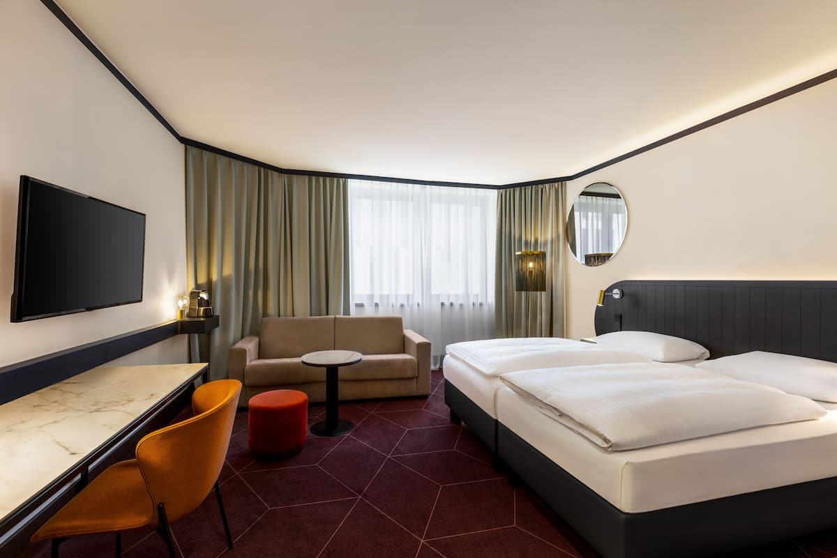 A hotel room with a bed, a sofa, a desk, and a TV.