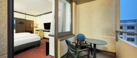 A hotel room with a bed, a small table, two chairs, a TV, and a window.