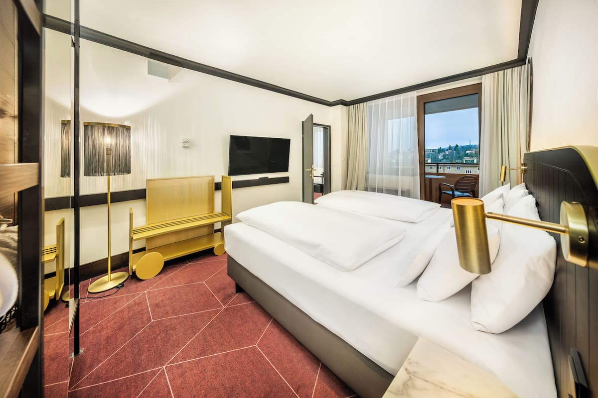 A hotel room with a large bed, a television, a desk with a lamp, and a view of the city.