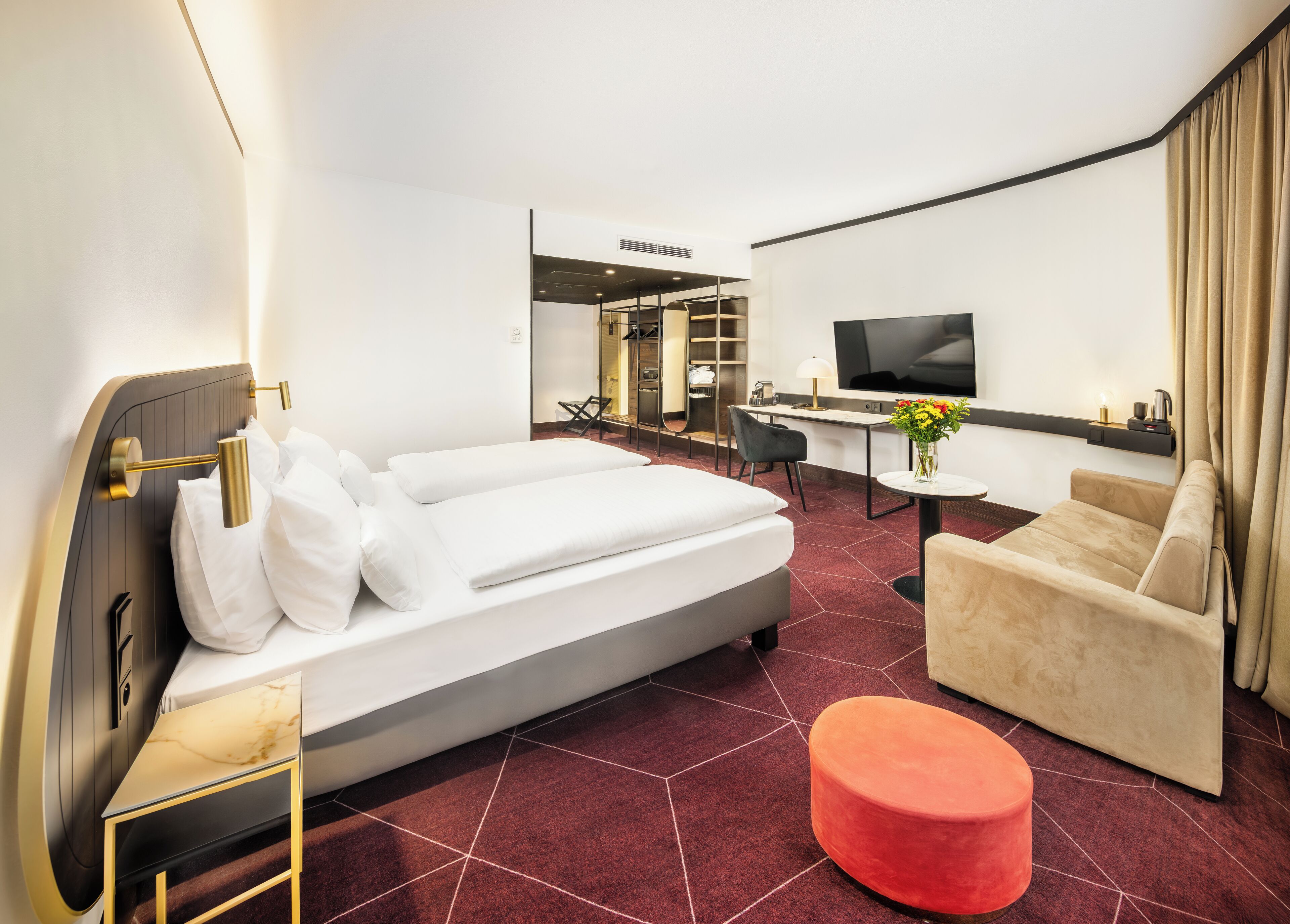 A modern hotel room with a large bed, a sofa, a small table, and a TV.