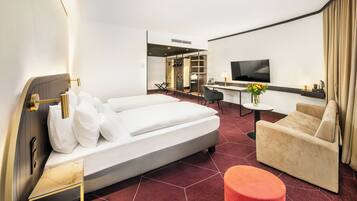 A modern hotel room with a large bed, a sofa, a small table, and a TV.