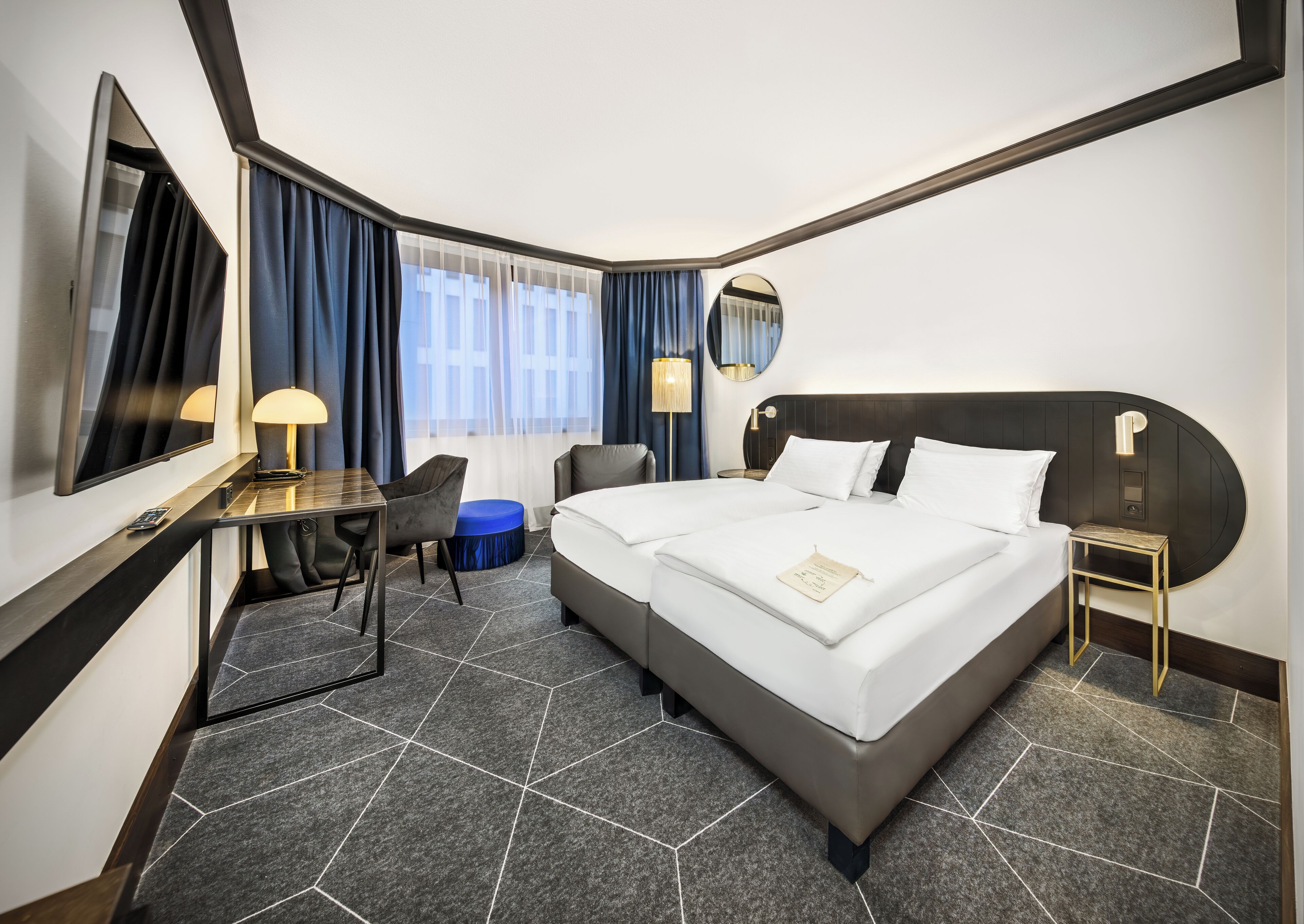 A hotel room with a large bed, a desk, a chair, a small table, and a mirror.