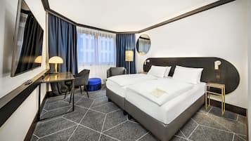 A hotel room with a large bed, a desk, a chair, a small table, and a mirror.
