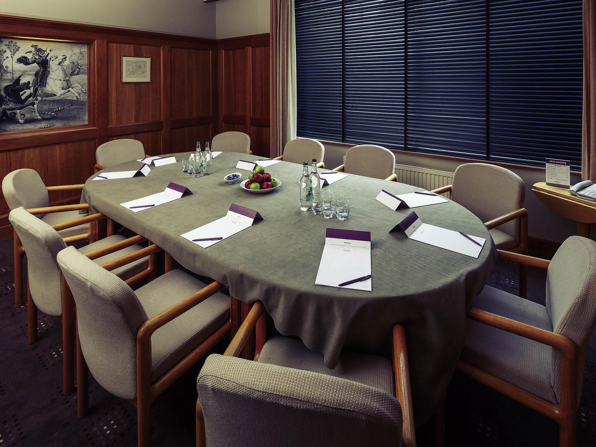 A conference room with a round table, chairs, name cards, water bottles, and a fruit bowl.