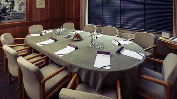 Un salón de conferencias con una mesa redonda, sillas, tarjetas de identificación, botellas de agua y un bol de fruta.