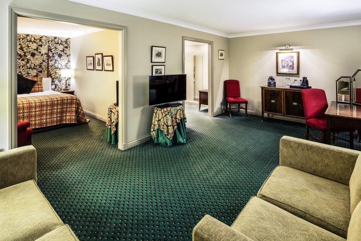 A hotel room with a bed, a television, a desk with a chair, and a red armchair.