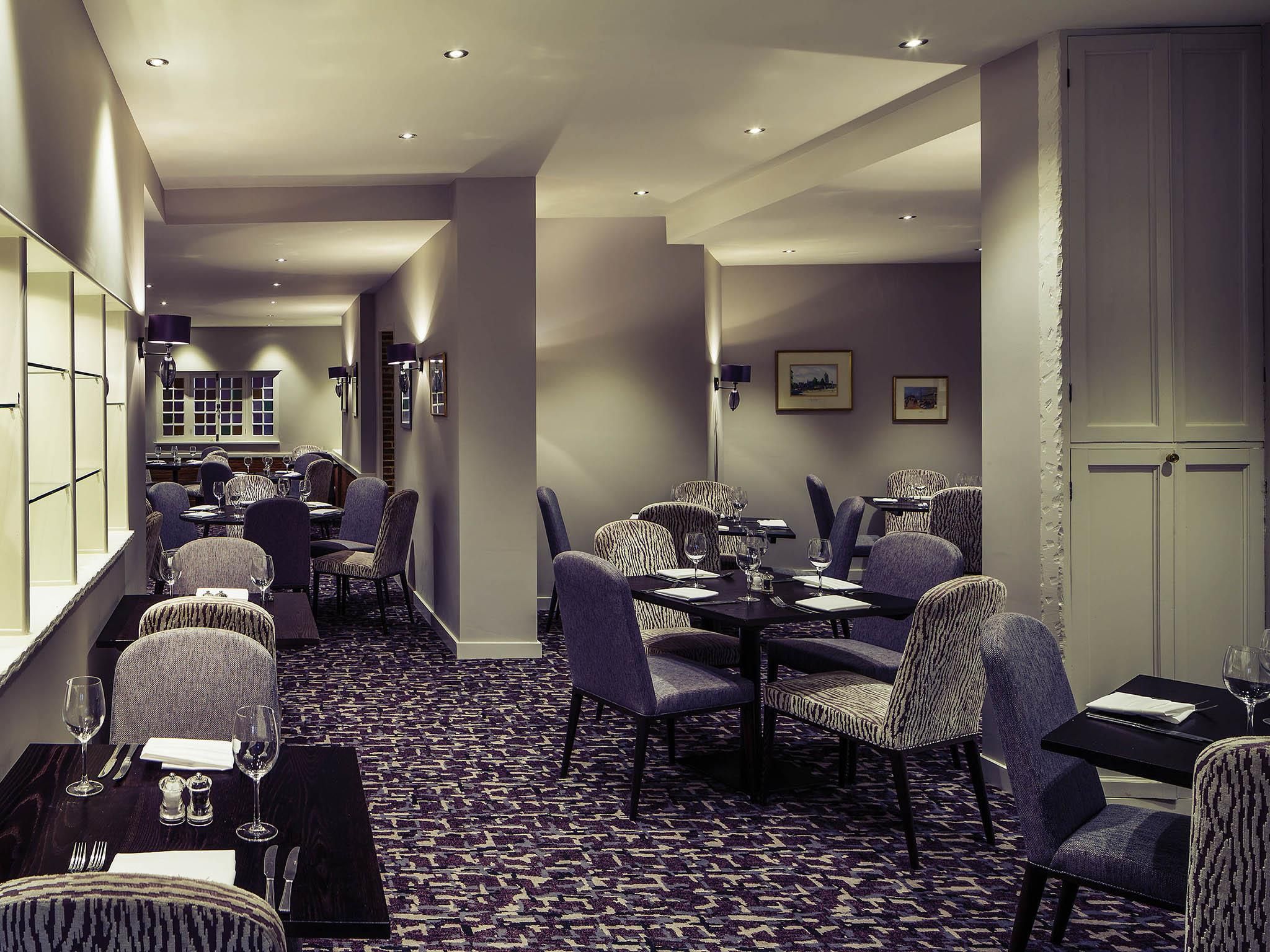 Un'area ristorazione di un hotel con un lungo tavolo, sedie e un tappeto decorato.