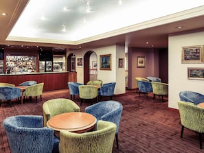Un vestíbulo de hotel con zona de bar, diferentes disposiciones de asientos y obras de arte en las paredes.