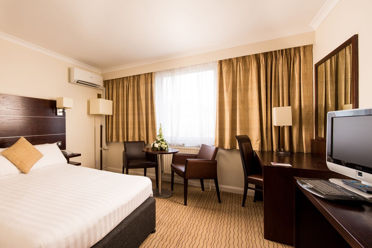 A hotel room with a large bed, a desk with a computer, a chair, and a television.