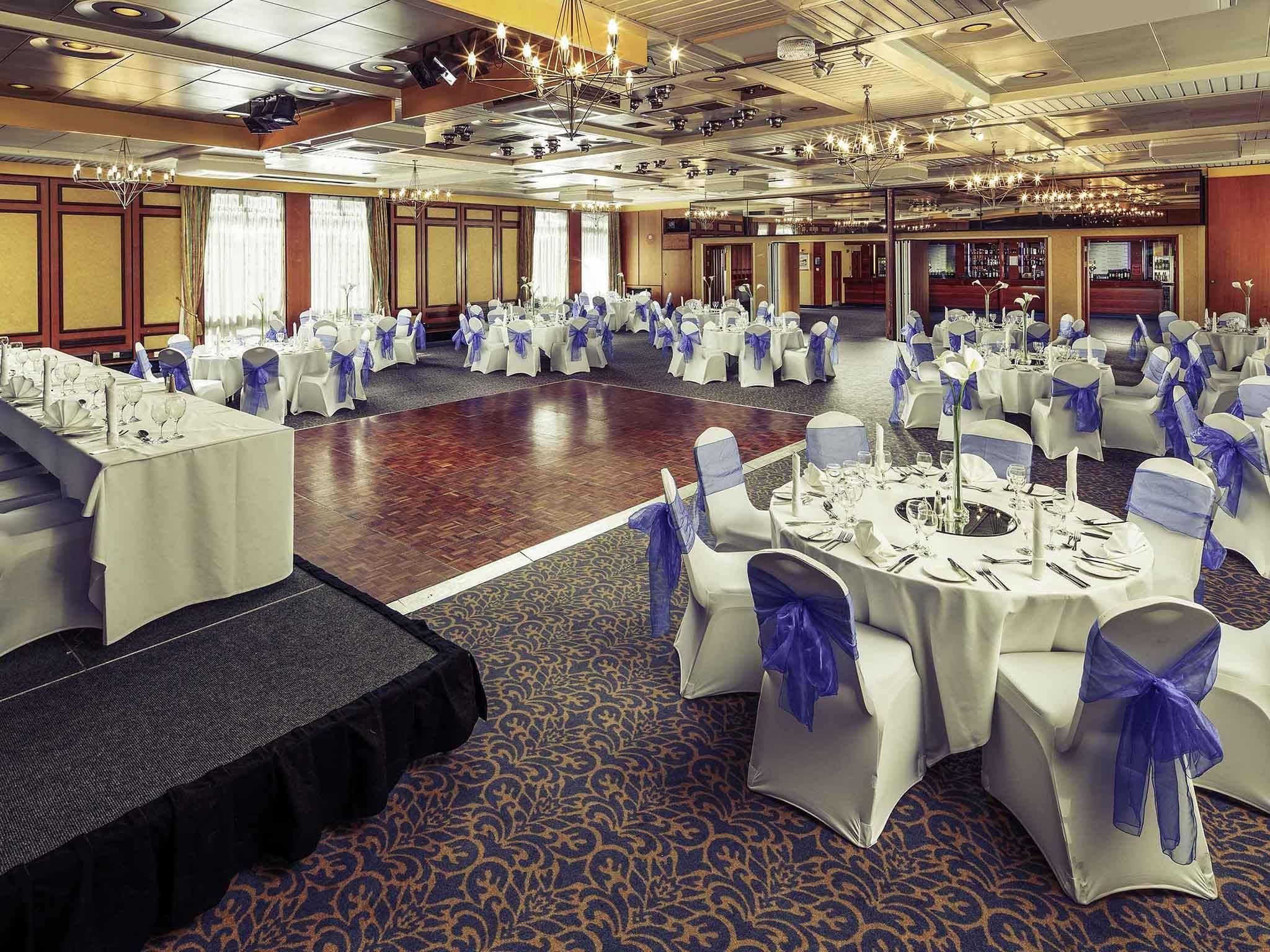 A banquet hall with round tables, white tablecloths, and blue chair sashes.