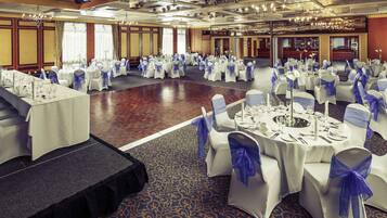A banquet hall with round tables, white tablecloths, and blue chair sashes.
