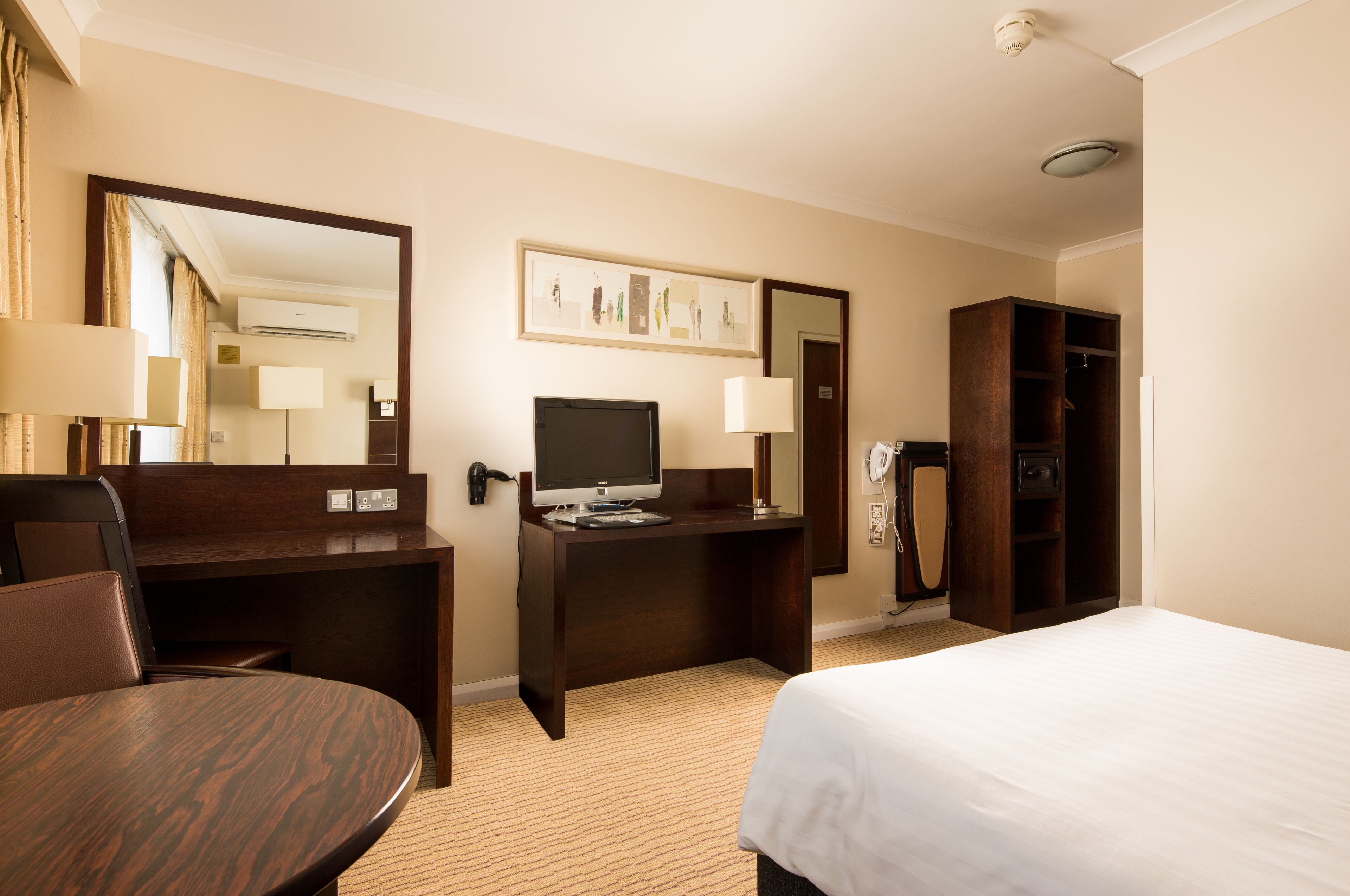 Une chambre d’hôtel comprenant un lit, un bureau avec un ordinateur, une chaise, une armoire et un miroir.