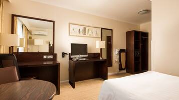 Une chambre d’hôtel comprenant un lit, un bureau avec un ordinateur, une chaise, une armoire et un miroir.