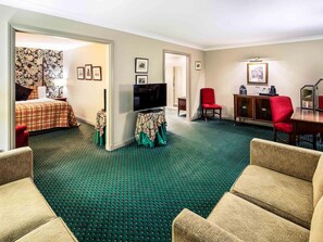 Habitación de hotel con cama, televisión, una silla roja, un armario de madera y alfombra verde.