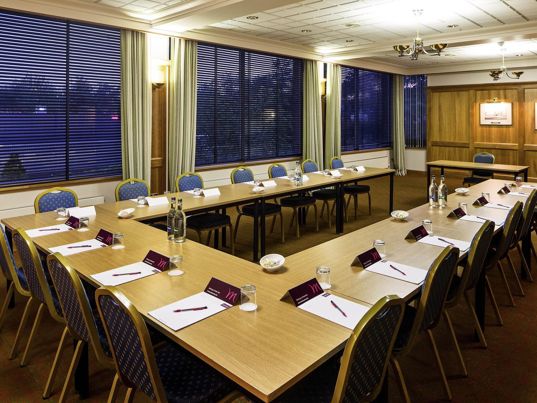 A conference room with a long table, chairs, name cards, water bottles, and a chandelier.
