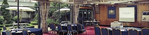 A conference room with tables and chairs, a projector screen, and a view of the outdoors. - Mercure Norwich Hotel (Norwich)