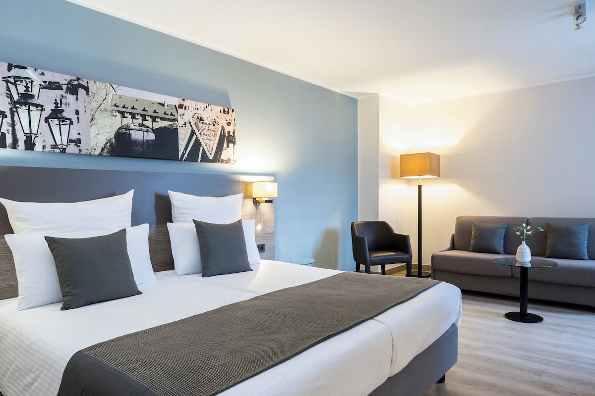 A hotel room with a large bed, a sofa, a chair, and a lamp.