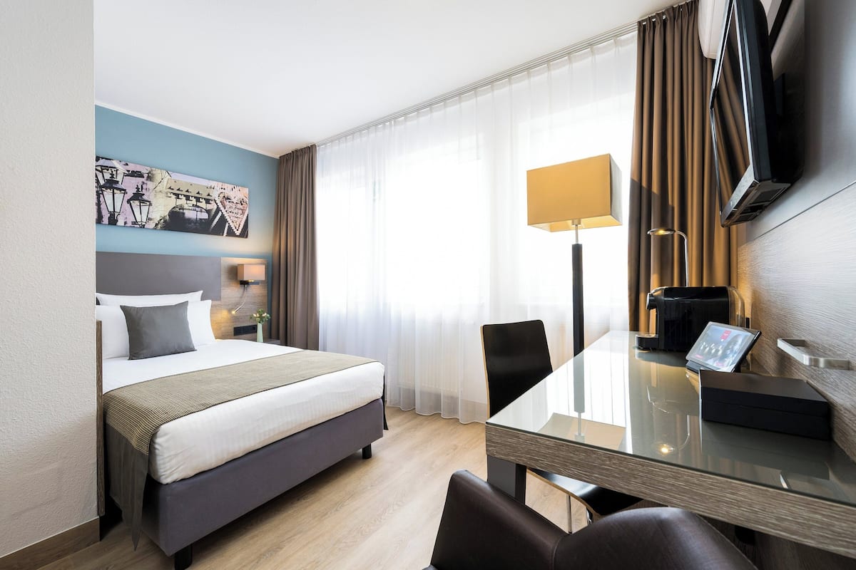 A hotel room with a bed, a desk with a chair, a television, and a lamp.