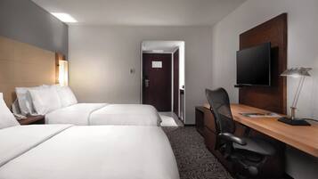 A hotel room with two beds, a desk, a chair, a television, and a door.