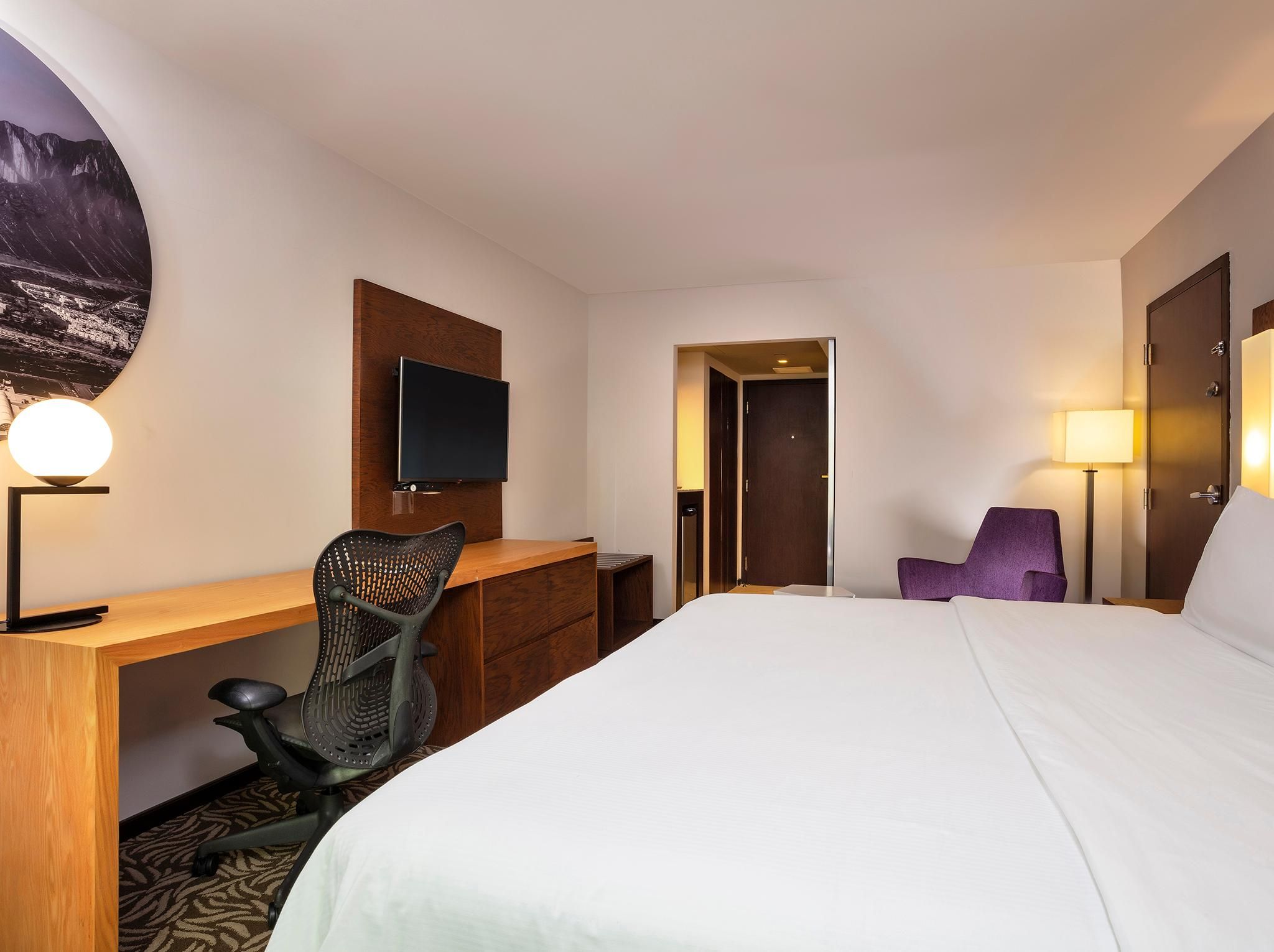 A hotel room with a bed, desk, chair, TV, and a door leading to a bathroom.