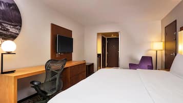 A hotel room with a bed, desk, chair, TV, and a door leading to a bathroom.