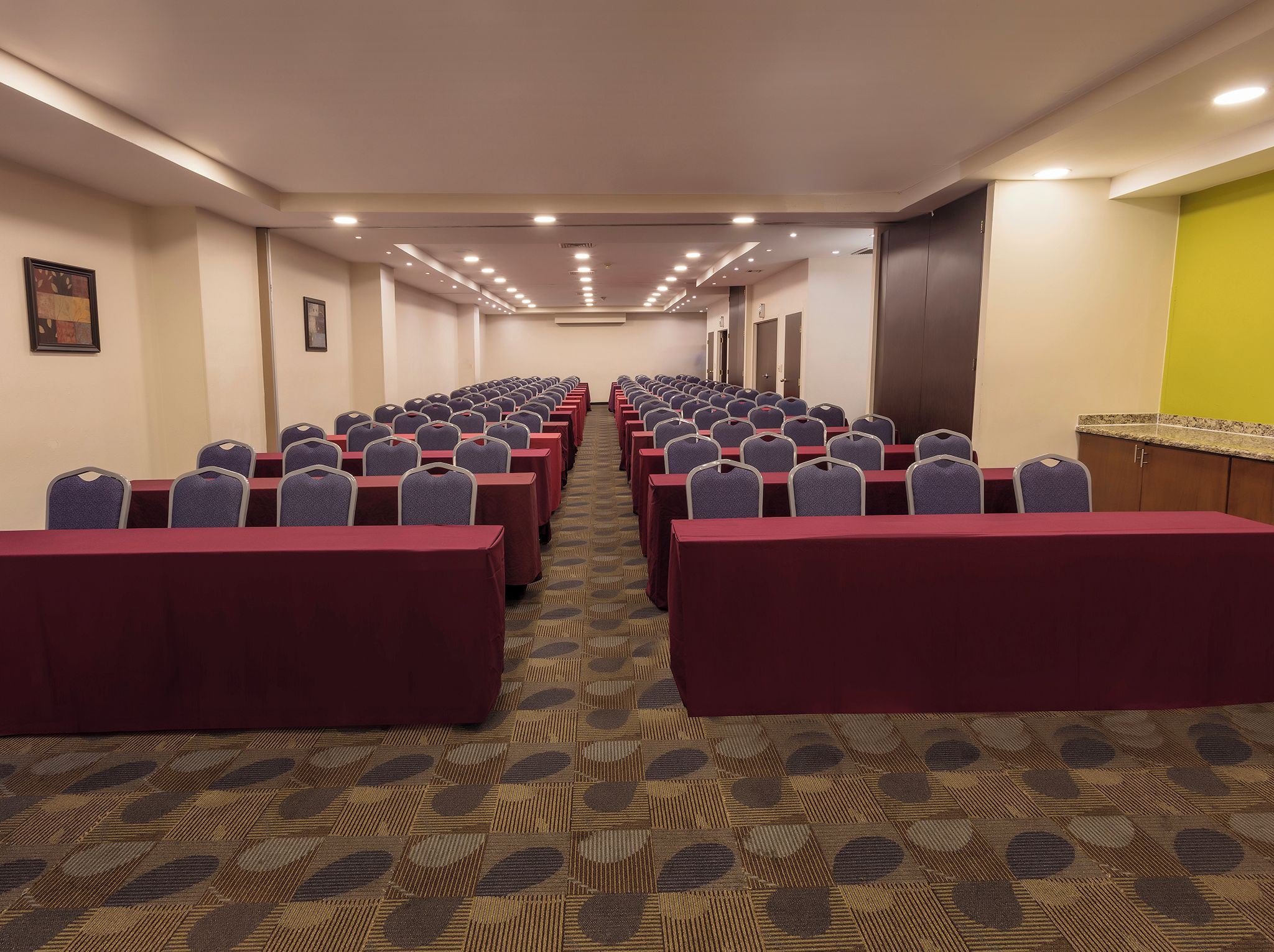 A conference room with rows of tables and chairs, carpeted floor, and a door on the right.