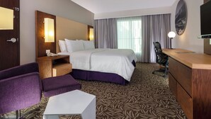 Une chambre d’hôtel équipée d’un lit, d’un bureau, d’une chaise, d’une petite table, d’un miroir et d’un téléviseur.