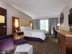 A hotel room with a bed, a desk, a chair, a small table, a mirror, and a television. - Krystal Urban Monterrey (Monterrey)
