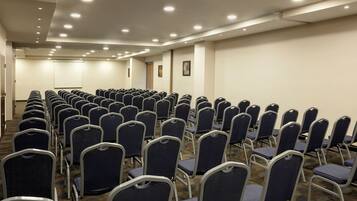 A conference room with rows of chairs, a projector screen, and a carpeted floor.