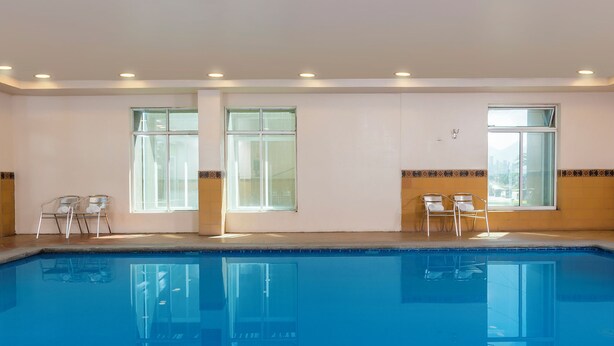 Une piscine à l’eau d’un bleu cristallin, entourée de murs blancs et dotée de deux fenêtres.