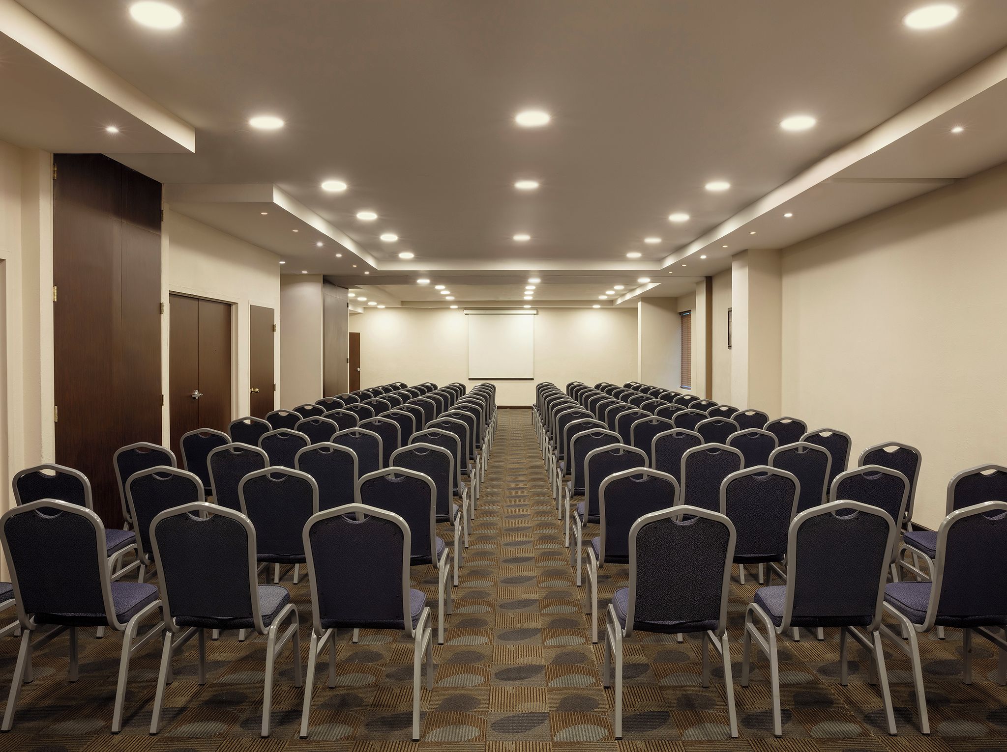 A conference room with rows of chairs, a carpeted floor, and ceiling lights.