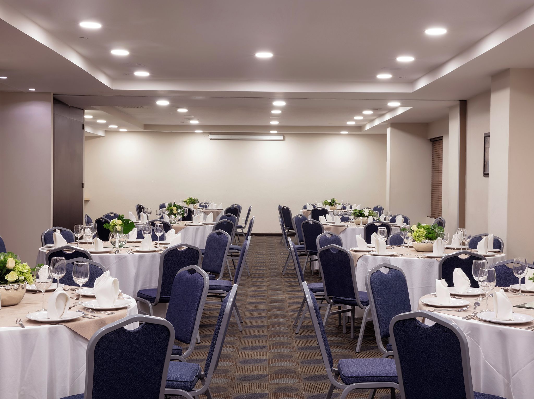 A conference room with rows of tables set for dining, equipped with chairs, tables, and centerpieces.