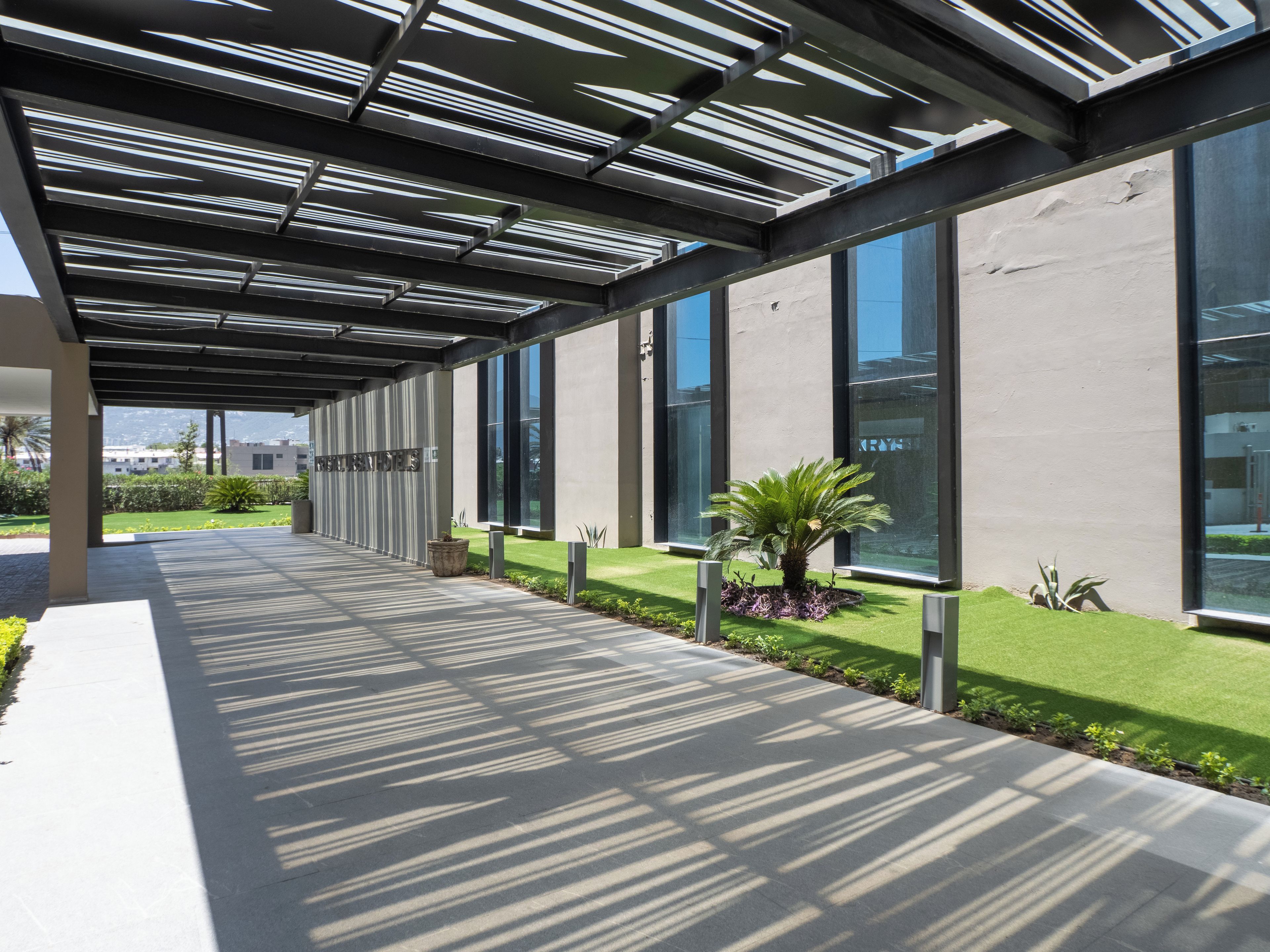 A covered walkway with a modern design, large windows, and a well-maintained lawn.