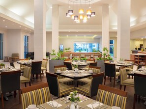 A spacious dining area with multiple tables and chairs, a central column, and a view of the outside through large windows. - Krystal Urban Monterrey (Monterrey)
