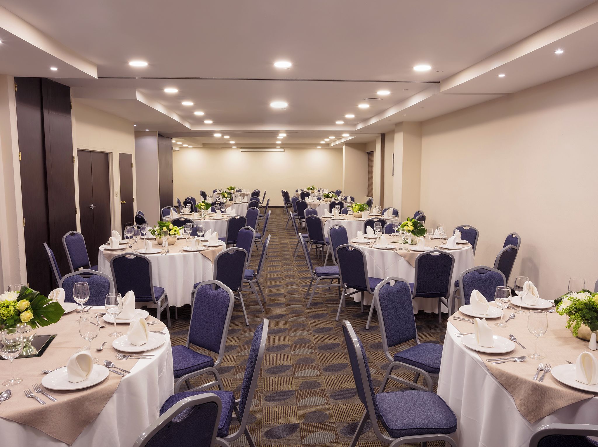A conference room with rows of tables, chairs, and a carpeted floor.
