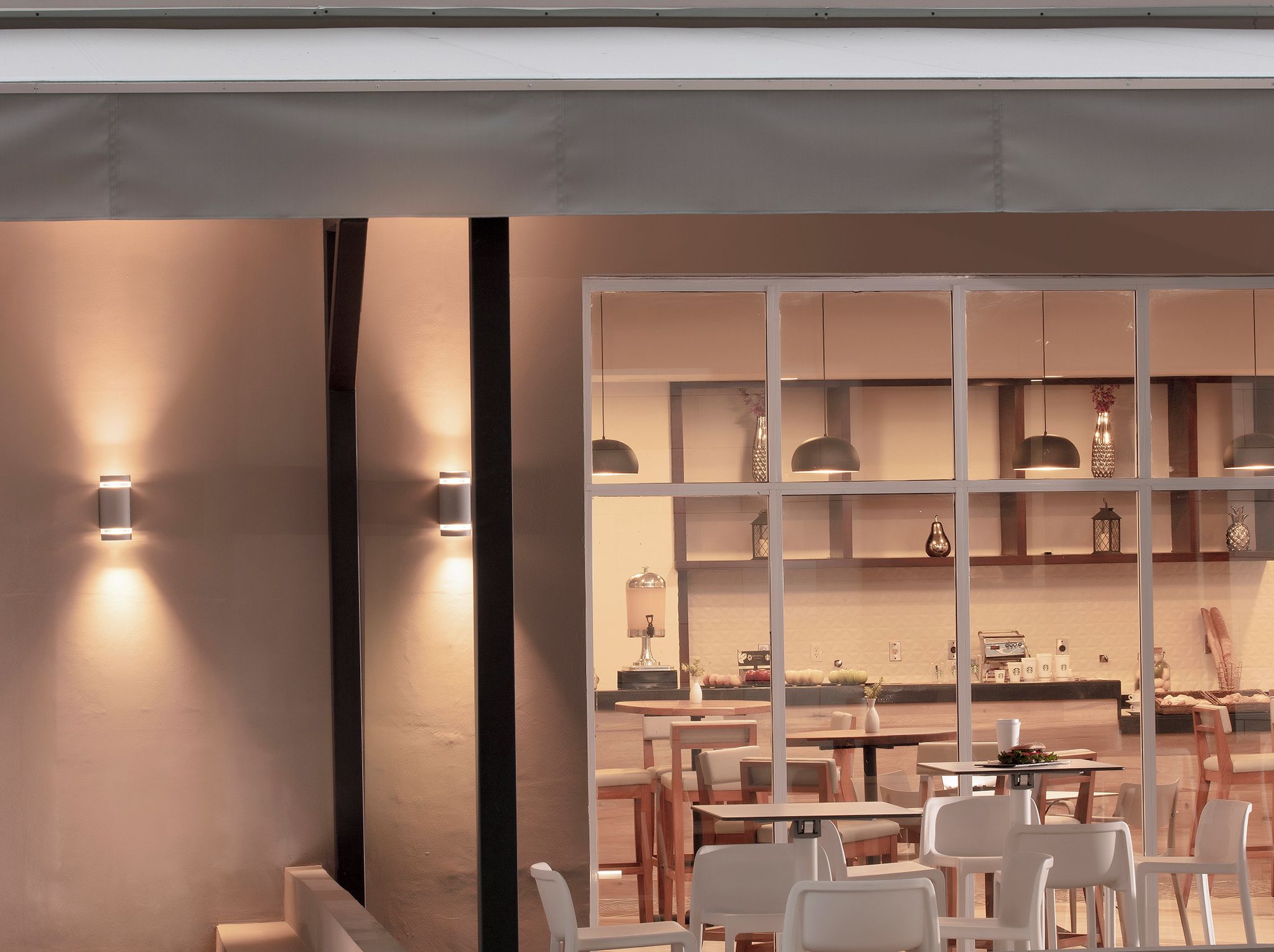 Un intérieur moderne avec un coin repas, des chaises blanches et une cuisine visible à travers une cloison en verre.