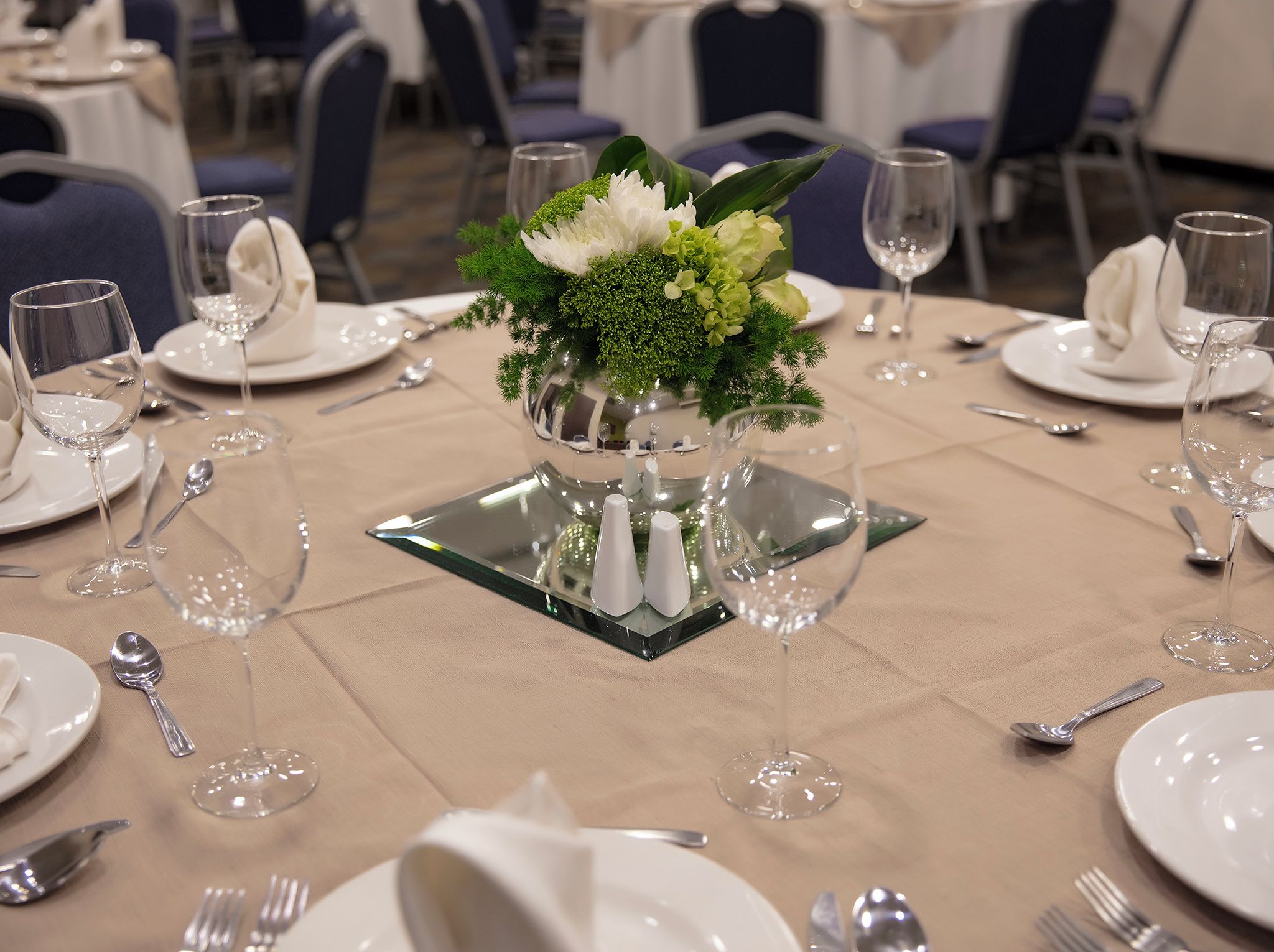 A table set for a formal dining occasion with a centerpiece of flowers and a reflective glass base.