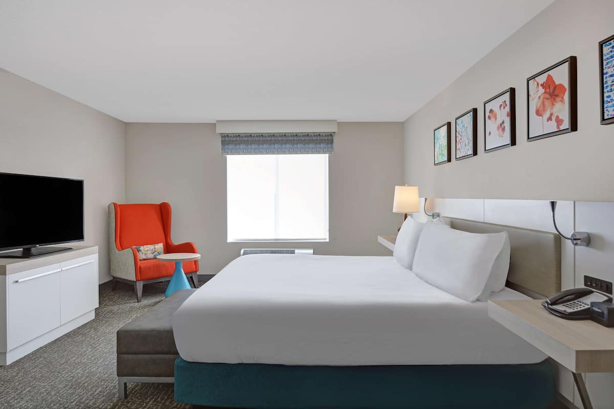 Une chambre d’hôtel avec un grand lit, une télévision, un bureau avec une lampe et une chaise.