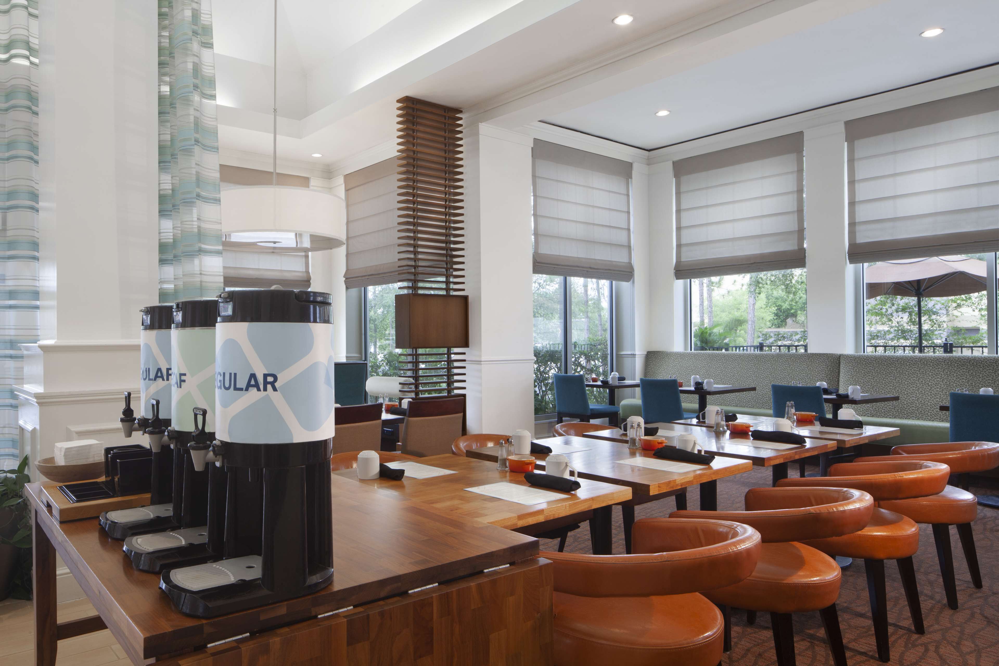 A modern hotel lobby with a long reception desk, multiple coffee machines, and comfortable seating areas.