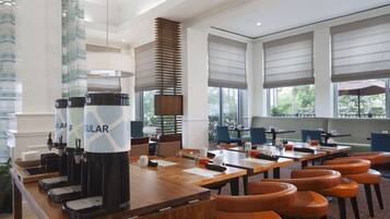 A modern hotel lobby with a long reception desk, multiple coffee machines, and comfortable seating areas.