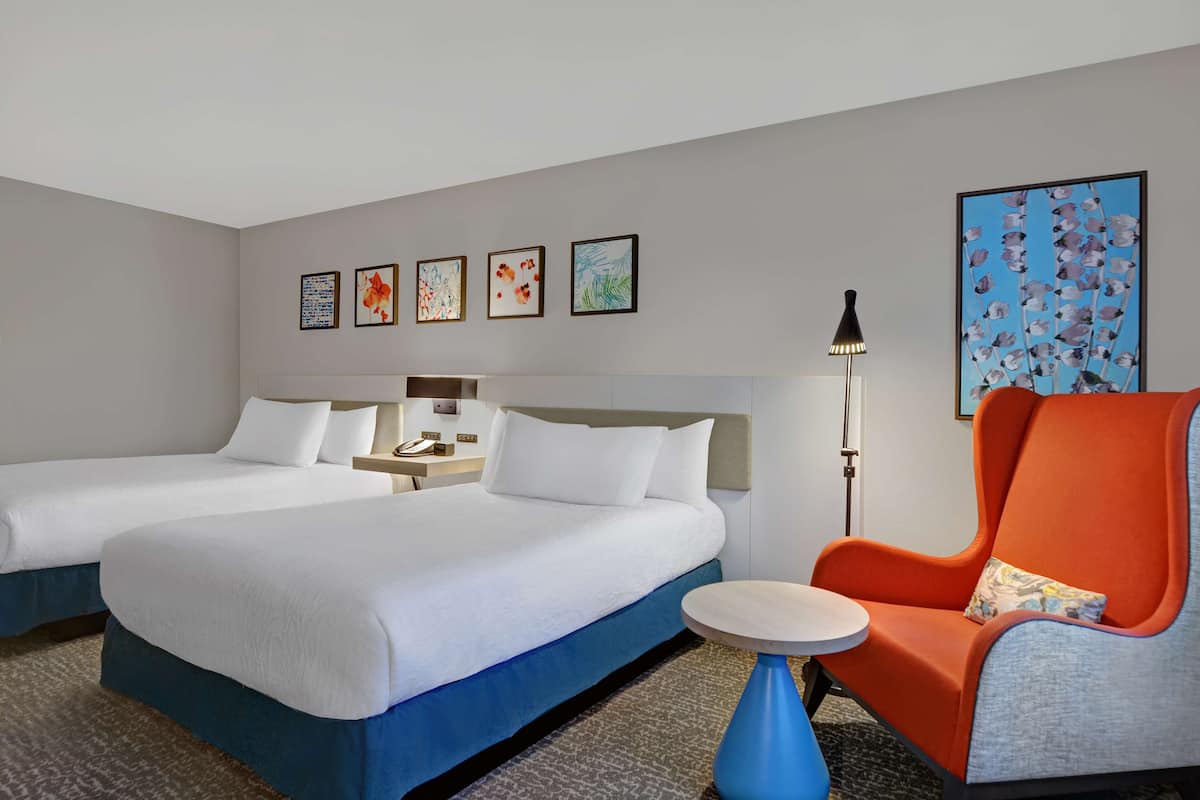 Une chambre d’hôtel avec deux lits, une table de chevet, une lampe et une chaise.