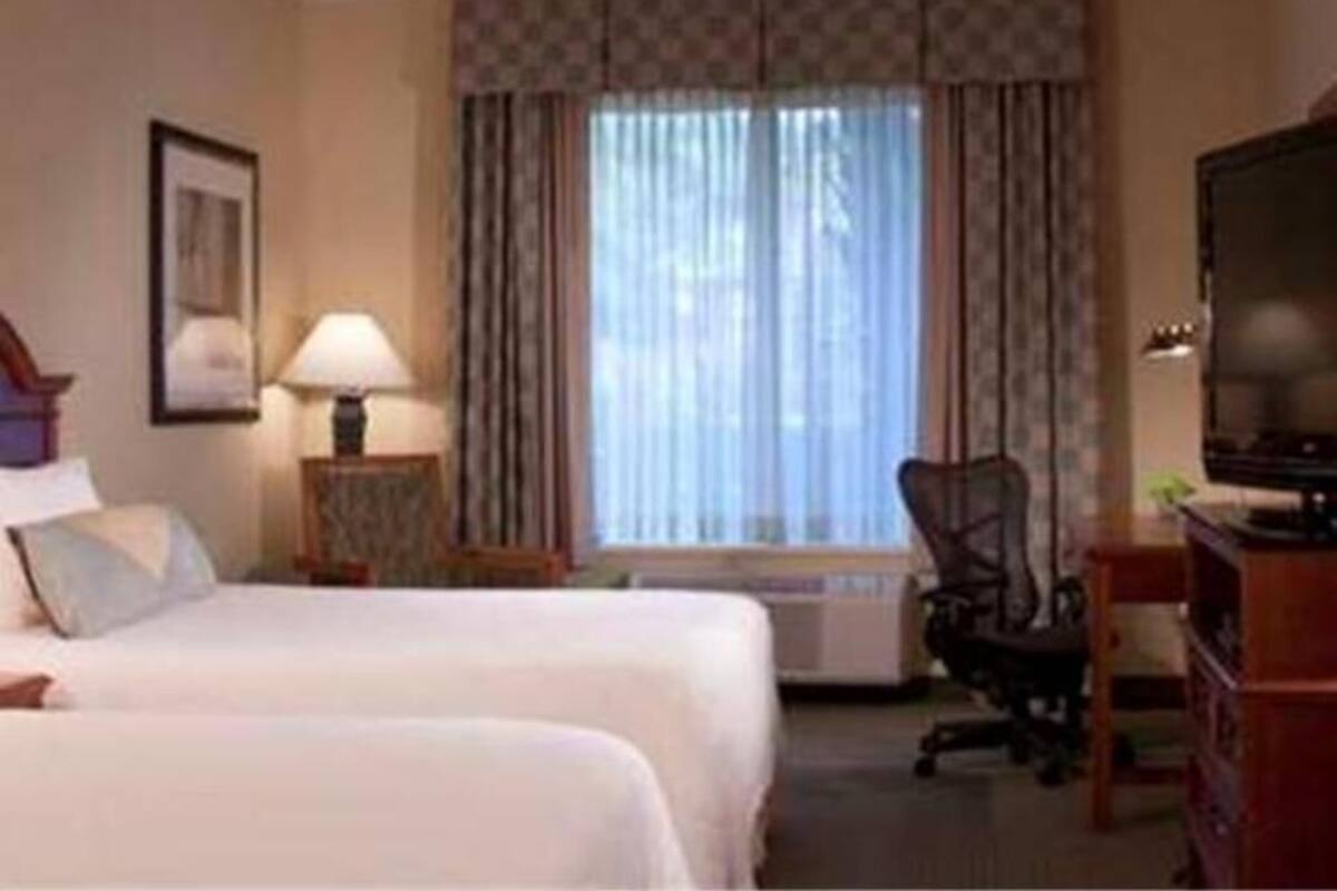 A hotel room with two beds, a desk, a chair, a television, and a window with curtains.