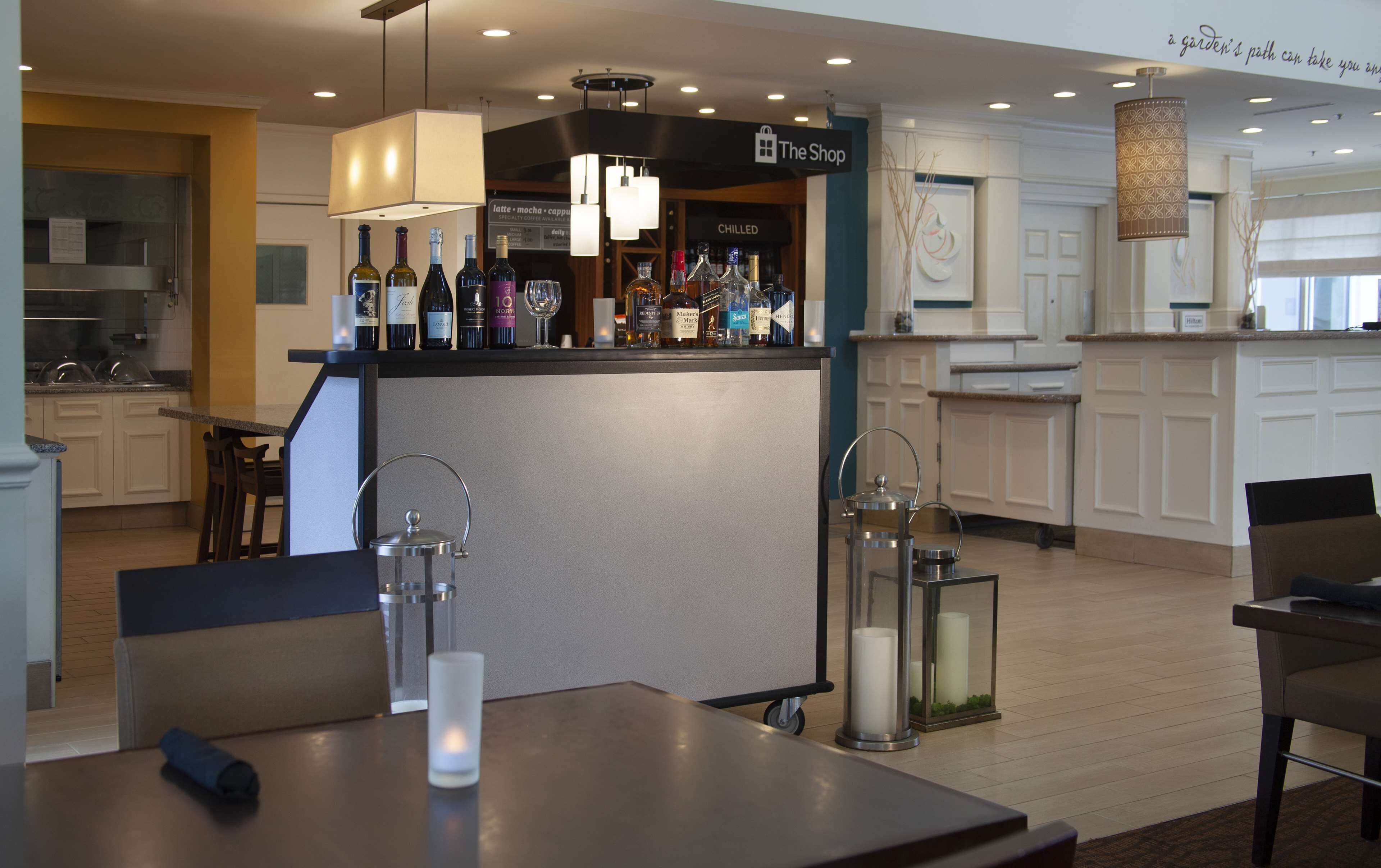 Een hotelbar met een toonbank waarop diverse flessen staan, een zithoek met tafels en stoelen, en een keuken op de achtergrond.