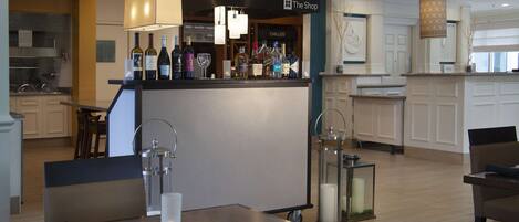 Een hotelbar met een toonbank waarop diverse flessen staan, een zithoek met tafels en stoelen, en een keuken op de achtergrond.