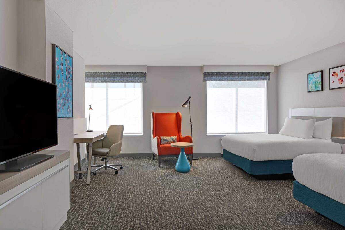 Une chambre d’hôtel équipée d’une télévision à écran plat, d’un bureau avec une chaise, d’un canapé, d’un lit et d’une lampe.