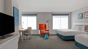 A hotel room with a flat-screen TV, a desk with a chair, a sofa, a bed, and a lamp.